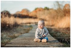 a baby boy sitting on a wooden walkway