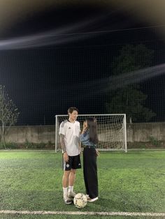 a man and woman standing next to each other in front of a soccer ball on a field