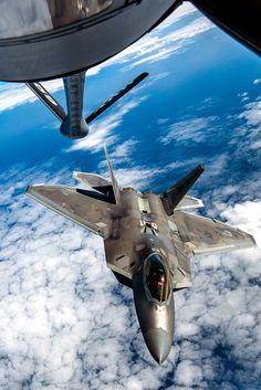 a fighter jet flying through the air over clouds and land below in front of an airplane