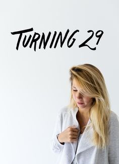 a woman standing in front of a white wall with the words turning 29 on it