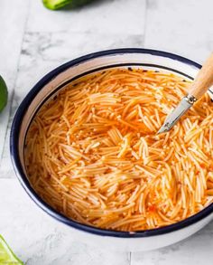 a bowl filled with shredded cheese next to limes