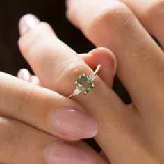 a woman's hand holding an engagement ring with a green stone on it,