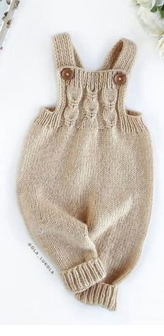 a knitted baby romper with buttons on the front and bottom, sitting next to flowers