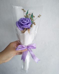 a person holding a bouquet of flowers in their hand with purple ribbon around it, on a white background