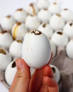 a person holding an egg in front of a bunch of white eggs with brown speckles on them