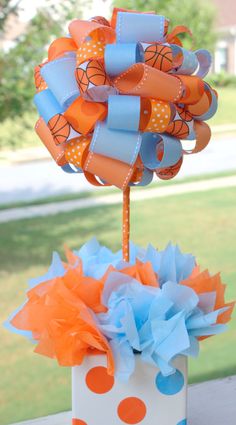 an orange, blue and white bow on top of a box with balloons in it