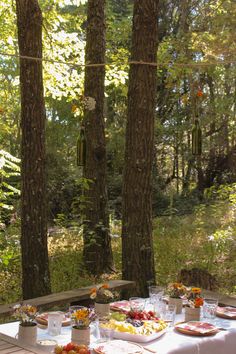 a picnic table with food and drinks on it in the woods next to some trees