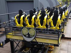 a row of yellow and black roller coasters with faces on the sides, sitting in front of a building