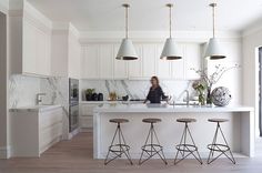 a large kitchen with white cabinets and marble counter tops, an island in the middle is flanked by three stools