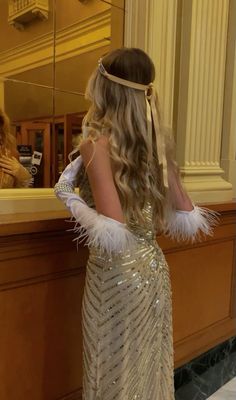 a woman standing in front of a mirror wearing a long dress with feathers on it