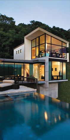 a modern house with a pool in the foreground and an outdoor dining area on the other side