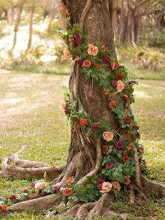 an old tree with vines and flowers growing on it's side in the grass