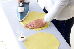 a woman ironing fabric on top of an ironing board with a yellow cloth