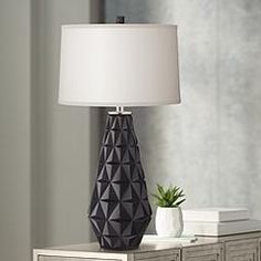 a table lamp sitting on top of a wooden dresser next to a white vase with a green plant in it