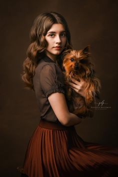 a woman holding a small dog in her hands and posing for the camera with dark background