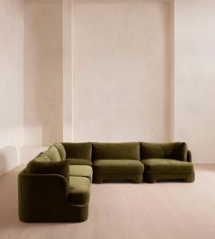 a large green couch sitting on top of a wooden floor next to a white wall