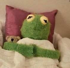 a green stuffed animal laying on top of a bed next to a pillow and teddy bear