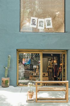 a store front with a wooden bench in the foreground and cactus on the other side