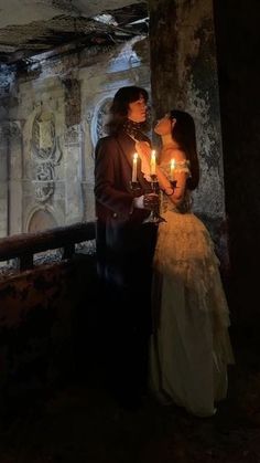 a man and woman standing next to each other holding candles in their hands while looking into the distance