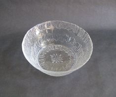 a clear glass bowl sitting on top of a gray tablecloth covered floor next to a black wall