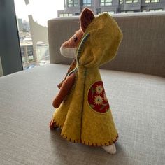 a stuffed animal is dressed in a yellow coat and standing on a table with a city view behind it