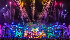 fireworks are lit up in the night sky above an illuminated concert stage with colorful lights