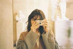 a woman taking a selfie in front of a statue holding a camera up to her face