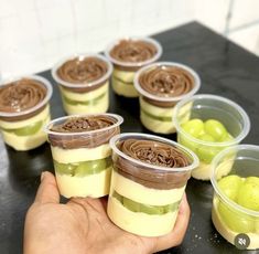 there are many desserts in plastic cups on the table with green apples around them