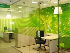 an office with green and yellow wallpaper, glass partitions and desks in the middle