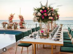 a table set up with flowers and place settings next to the swimming pool at sunset