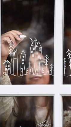 a woman is drawing on the window glass with white marker and pen while she looks out