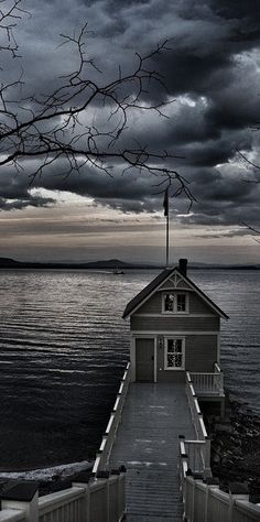 a house sitting on top of a pier next to the ocean under a cloudy sky