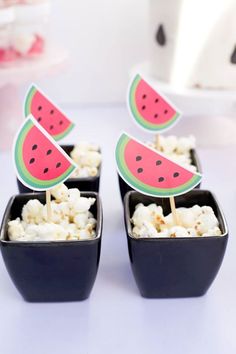 some watermelon slices are sitting in small black containers with marshmallows