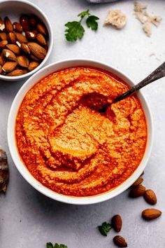 two bowls of hummus and almonds on a white surface with nuts in the background