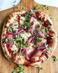 a pizza topped with meat and veggies on top of a wooden cutting board