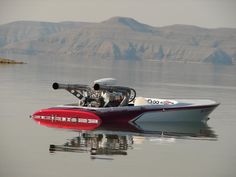 a red and white speed boat on water with mountains in the background