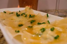 a white plate topped with pasta covered in cheese and green onions next to a glass of wine