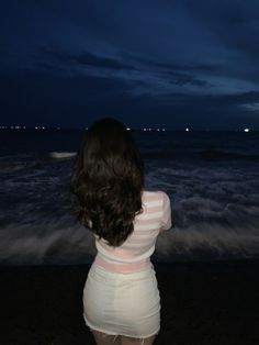 a woman standing on top of a beach next to the ocean under a cloudy sky