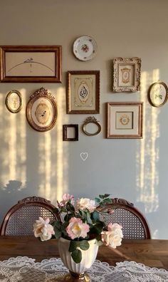 there is a vase with flowers on the table in front of many pictures and frames