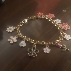 a gold bracelet with flowers and charms attached to it, sitting on a wooden table