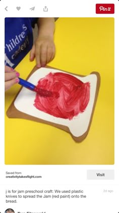 a child is painting on a piece of paper with red paint and a blue brush