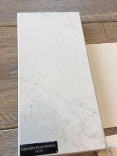 a white marble counter top with a black label on the bottom and brown wood flooring behind it