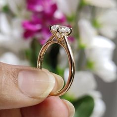 a person holding a gold ring with two diamonds on it and flowers in the background