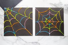 two spider webs are drawn on black paper with colored crayons in front of them