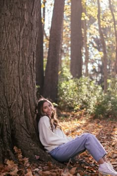 a woman sitting on the ground next to a tree