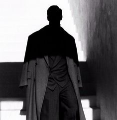 a black and white photo of a man in a suit standing next to some stairs