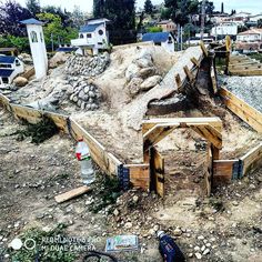 an unfinished wooden structure sitting on top of a dirt field next to a pile of rocks