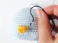 a hand holding a needle and thread over a crocheted hat with a small yellow object on it