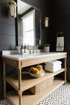 a white sink sitting under a mirror next to a wooden shelf with towels on it