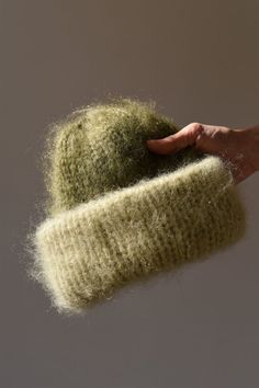 a hand is holding up a green knitted hat that has been made from wool